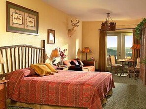 Una habitación de hotel con una cama grande, una cabeza de ciervo montada, cuadros en la pared y vistas al exterior a través de la ventana.
