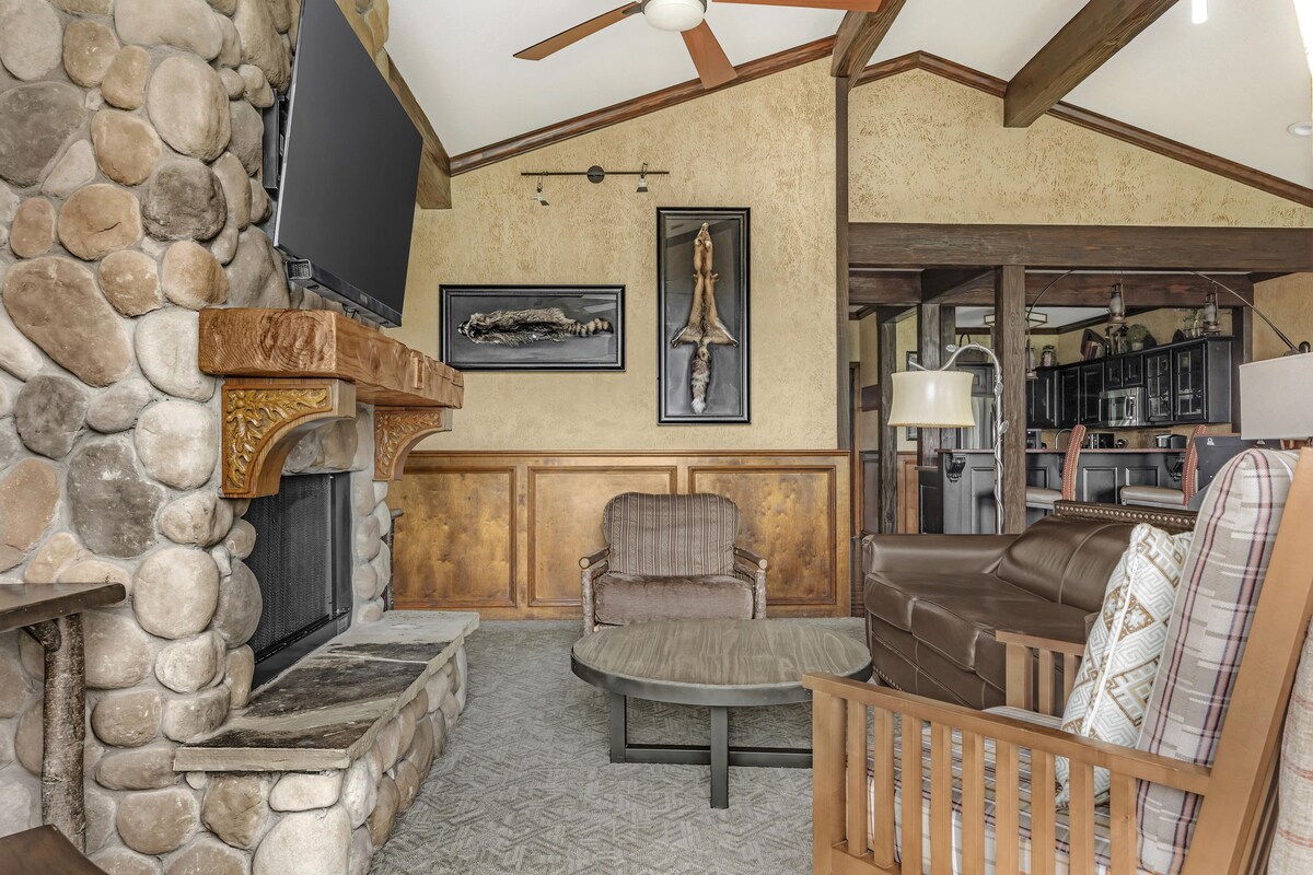 A stone fireplace, a television, a framed animal skull, a patterned armchair, a leather sofa, and a wooden bench.