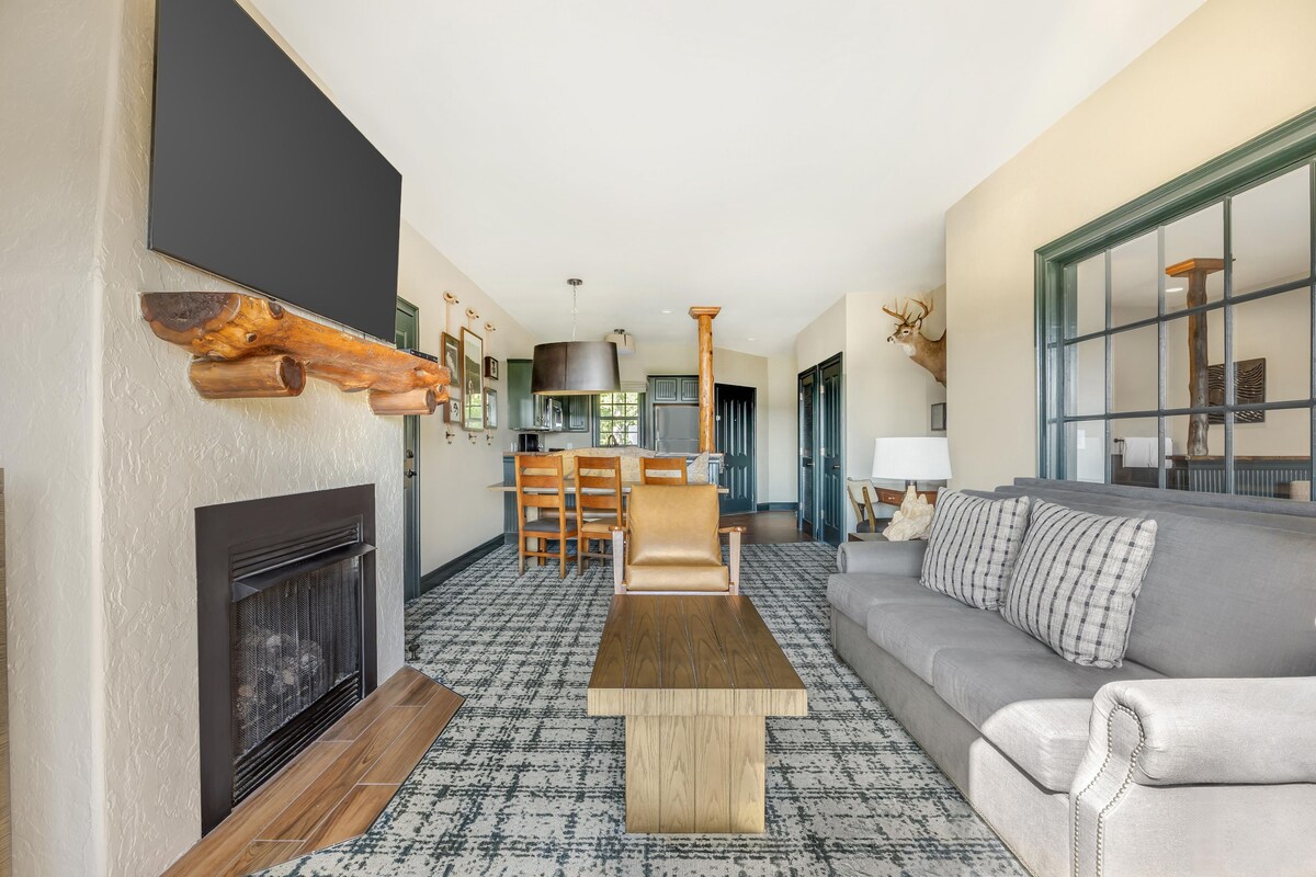 A modern living room with a fireplace, a sofa, a coffee table, and a dining area.