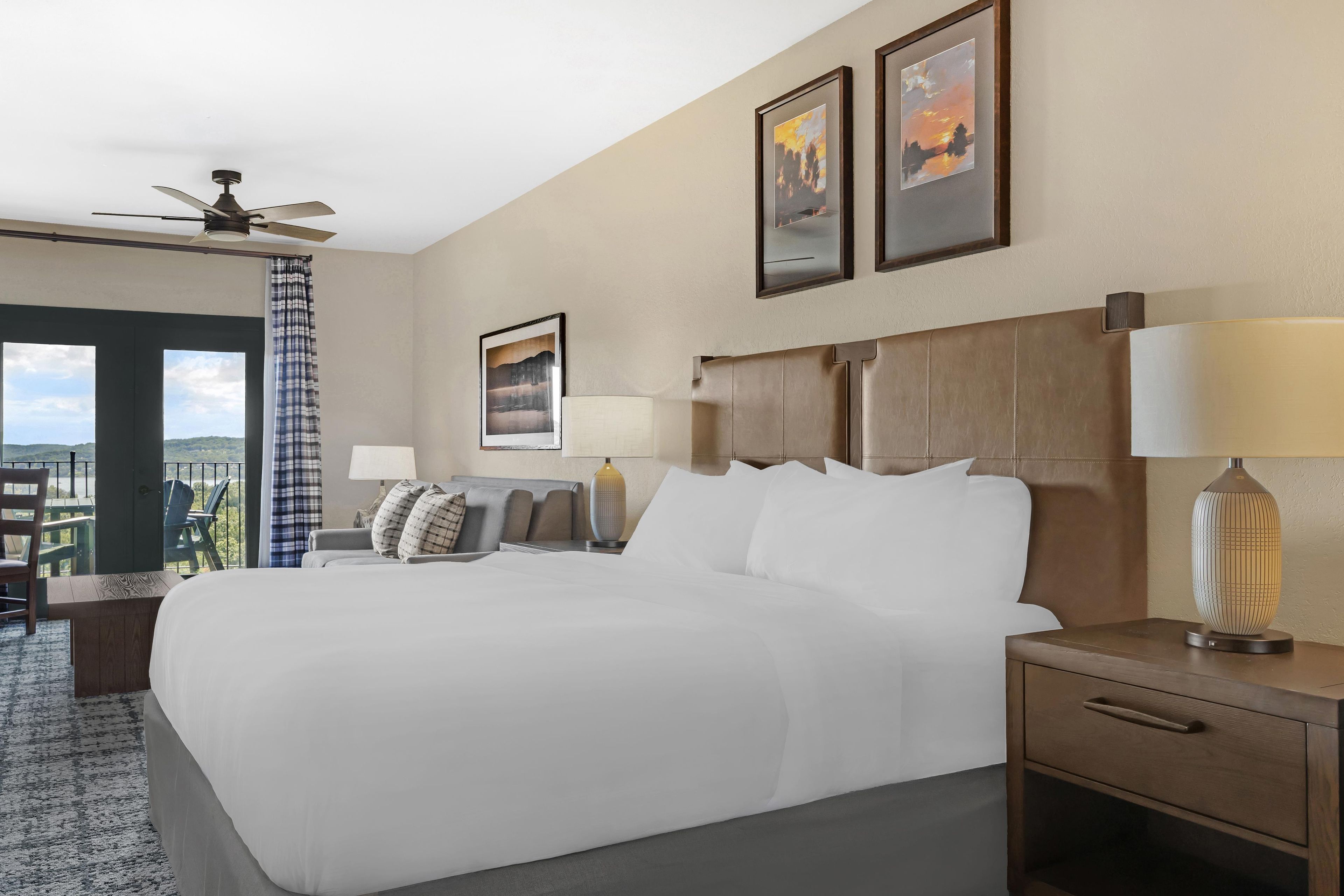 A hotel room with a large bed, two bedside lamps, a ceiling fan, and a view of the outdoors.
