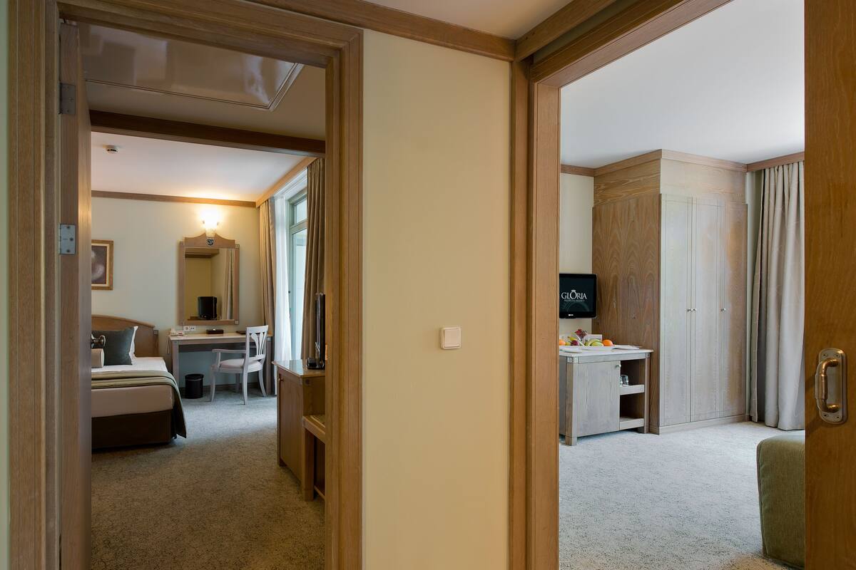 Quarto de hotel com cama, escrivaninha, cadeira, televisão, guarda-roupa e uma pequena mesa com frutas.
