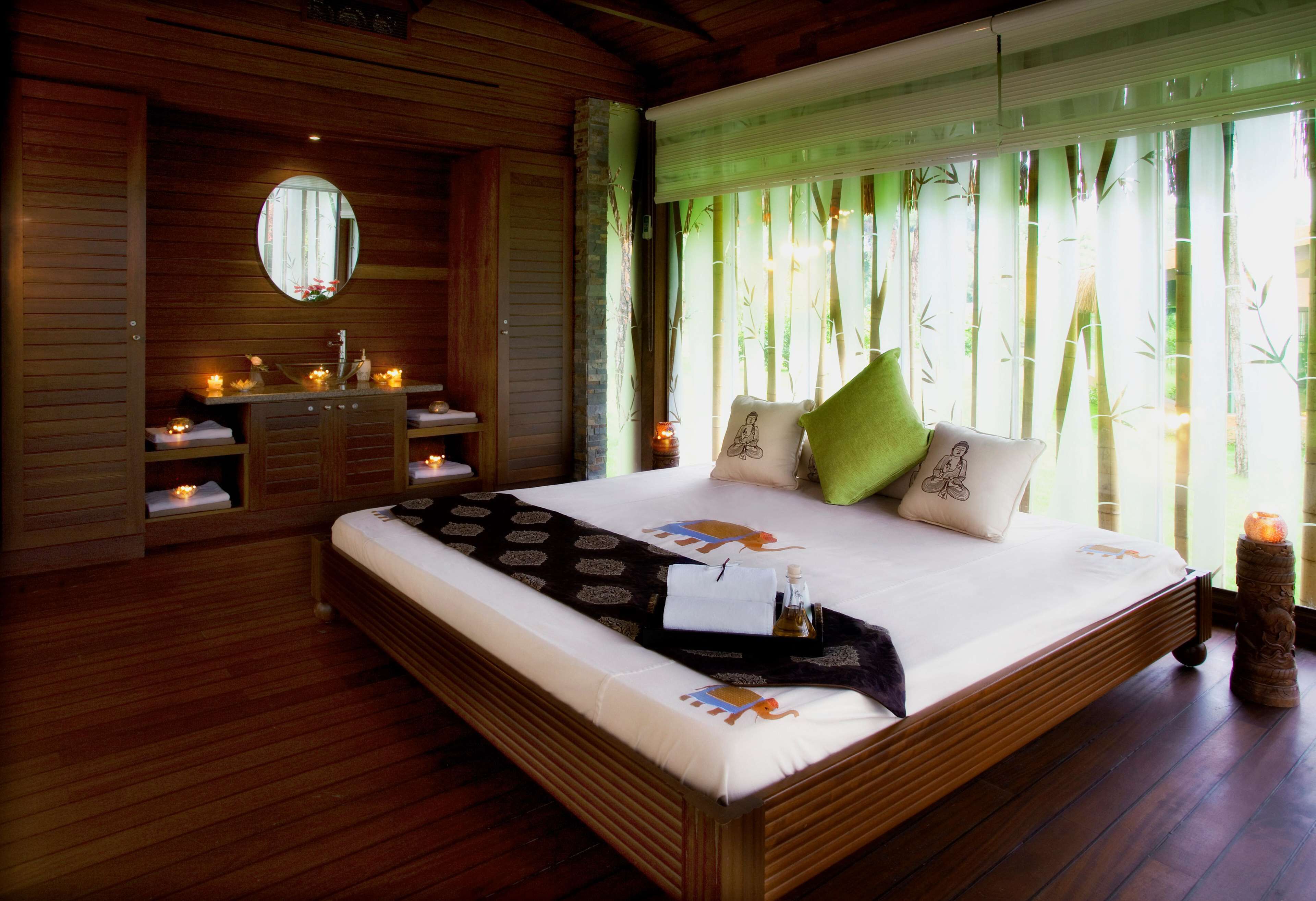 Dormitorio con piso de madera, una cama grande, una mesita de noche, un espejo y una ventana con cortinas de bambú.