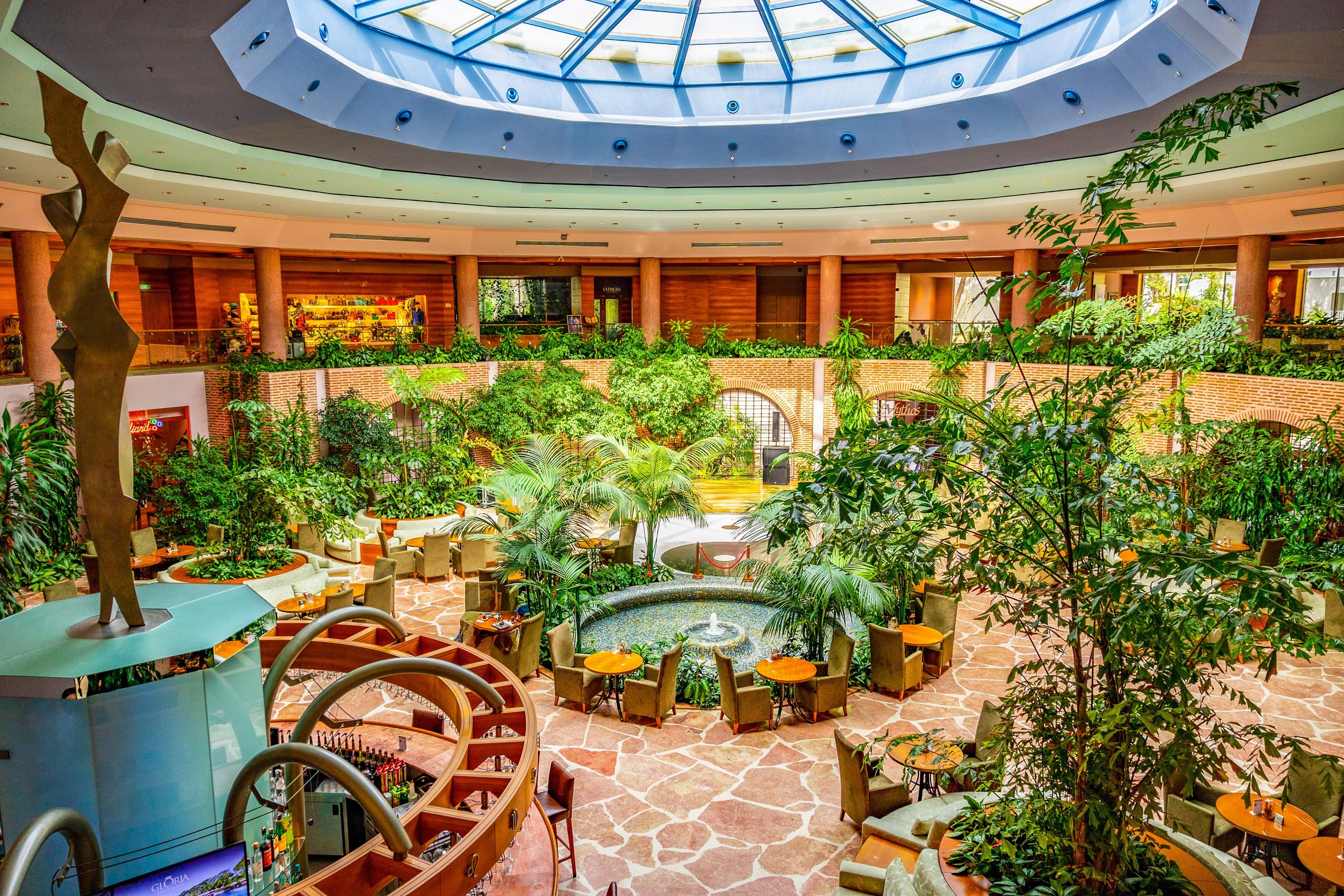 A hotel atrium with a central fountain, seating areas, and a spiral staircase.