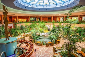 Un vestíbulo de hotel con una fuente central, zonas de estar y una escalera de caracol.