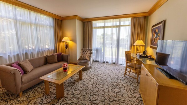 A hotel room with a sofa, armchair, dining table, and TV.