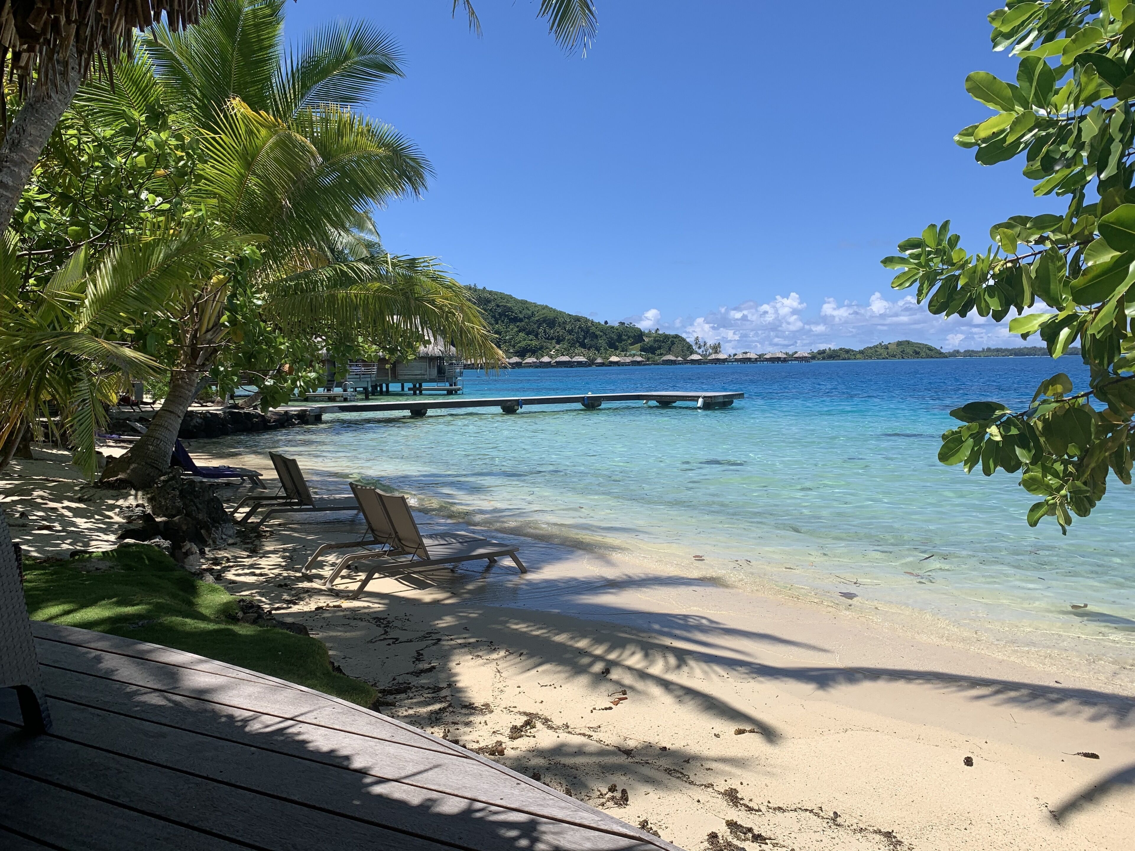 A beach with clear turquoise water, lounge chairs, and a wooden deck.