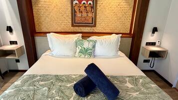 Habitación de hotel con una cama grande, ropa de cama blanca, colcha de hojas verdes, toalla azul y una obra de arte enmarcada sobre la cama.