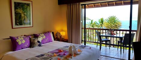A hotel room with a bed, a balcony with a table and chairs, and a view of the sea.
