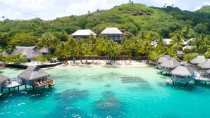 Un resort tropical con bungalows sobre el agua, aguas turquesas cristalinas y abundante vegetación.