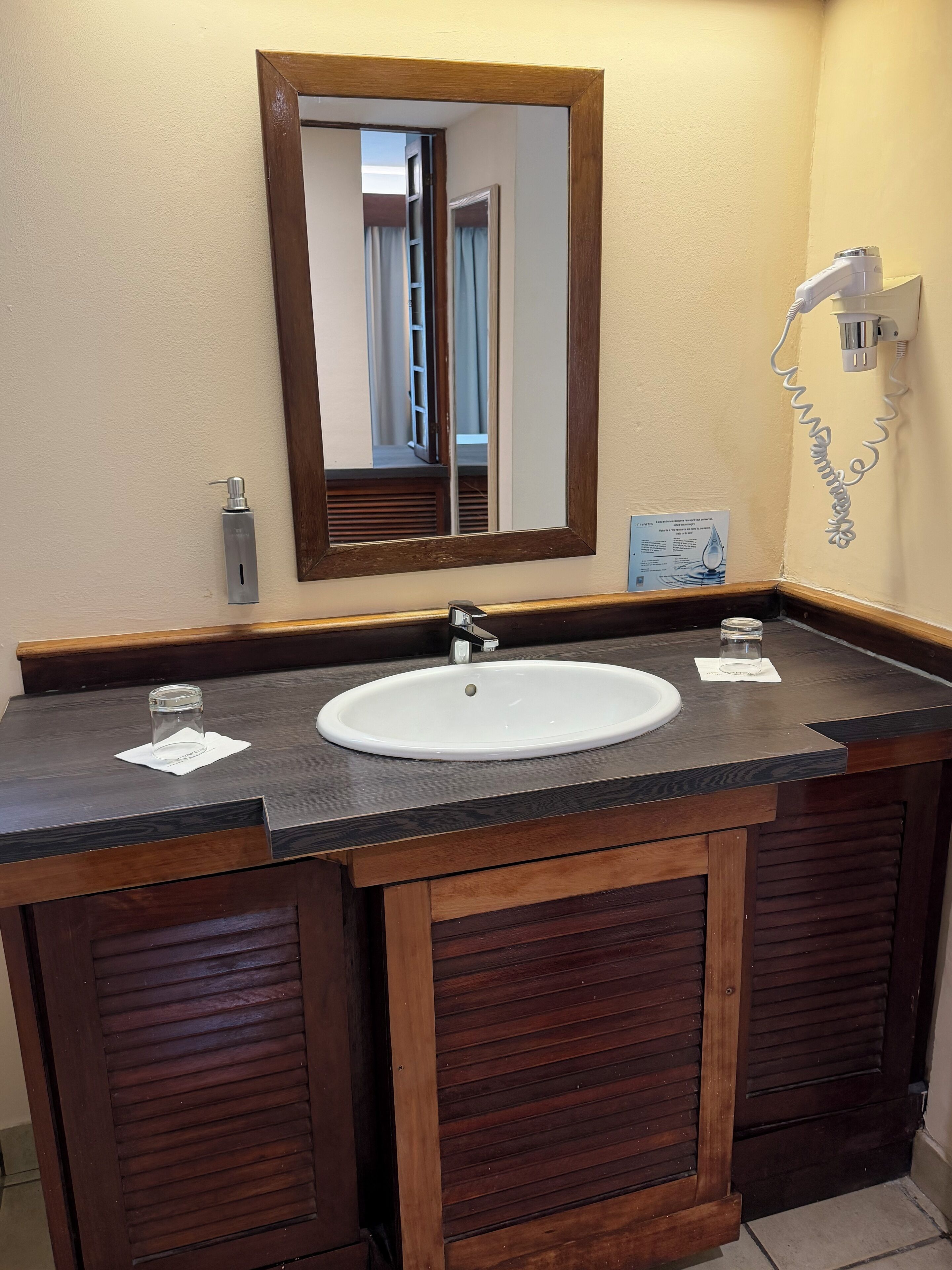A bathroom with a large mirror, a white sink, and wooden cabinets.