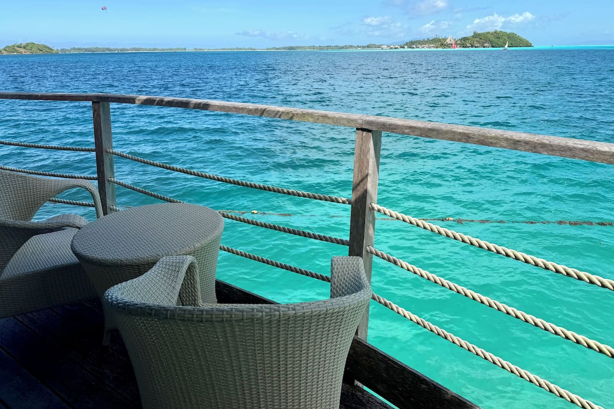 A deck with wicker chairs and a wooden railing overlooking turquoise waters.