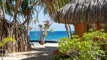 Un chalet de plage avec un toit de chaume, entouré de palmiers et offrant une vue sur l’océan.