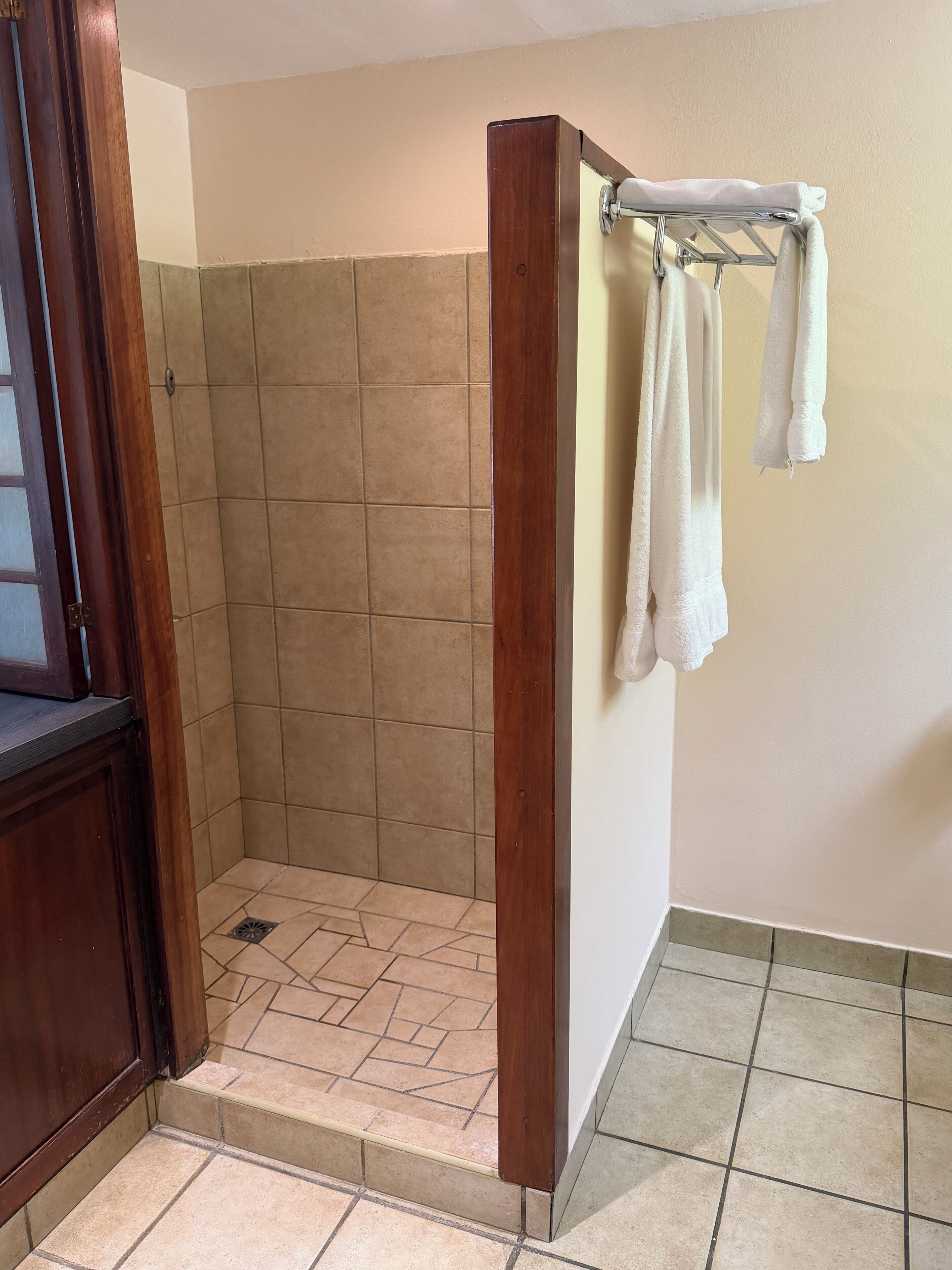 A shower area with tiled walls and floor, a wooden door frame, and a towel rack with towels.