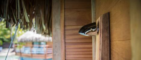 A wooden door with a metal handle, a thatched roof, and a wooden fence in the background.