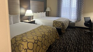 Habitación de hotel con dos camas, un escritorio, una silla y un ventanal con cortinas estampadas.