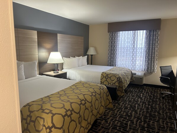 Habitación de hotel con dos camas, un escritorio, una silla y un ventanal con cortinas estampadas.