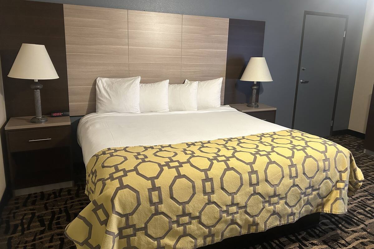 A hotel room with a large bed, two bedside tables with lamps, a wooden headboard, and a door.
