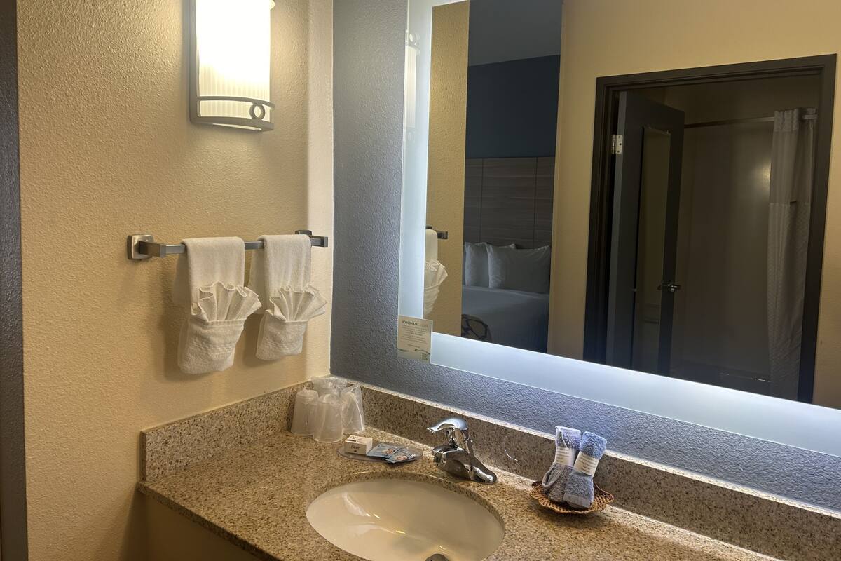 A bathroom with a granite countertop, a white sink, a mirror, and a towel rack with two towels.