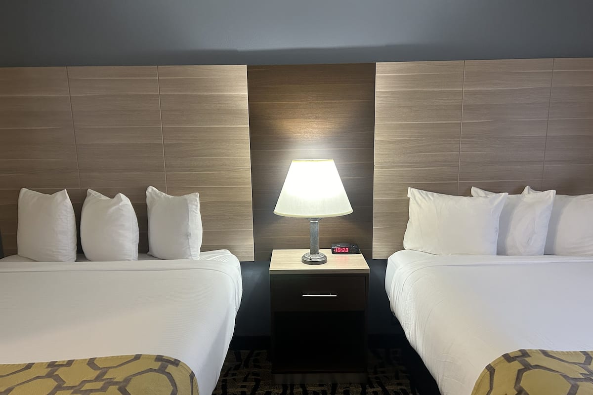 A hotel room with two beds, a nightstand with a lamp, and a digital clock.