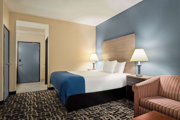 Une chambre d’hôtel avec un lit, deux tables de chevet avec des lampes, un fauteuil à rayures et une moquette à motifs.