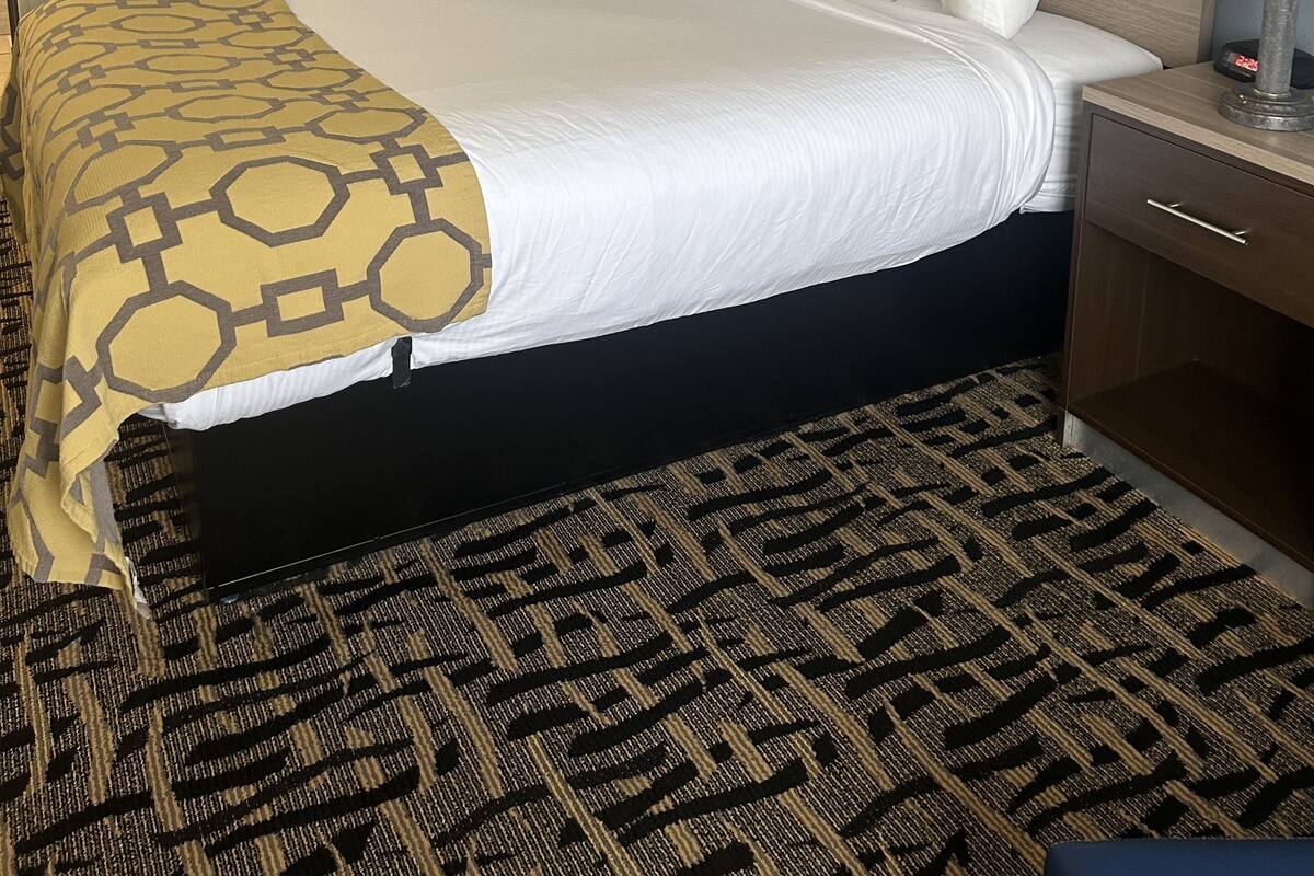 Habitación de hotel con una cama grande, dos mesitas de noche, un cabecero y una alfombra estampada.