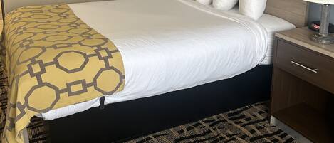 A hotel room with a large bed, two bedside tables, a headboard, and a patterned carpet.