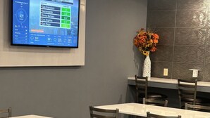 Un restaurante con una pantalla grande mostrando el pronóstico de lluvias en California. Hay varias mesas y sillas dispuestas para comer.
