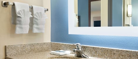 Un baño con encimera de granito, un lavamanos blanco, un espejo y dos toallas blancas colgadas en un tendedero de metal.