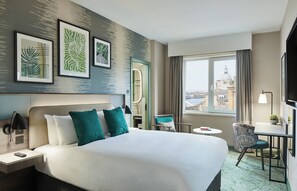 Quarto de hotel com uma cama grande, uma escrivaninha, uma cadeira e vista para a cidade.