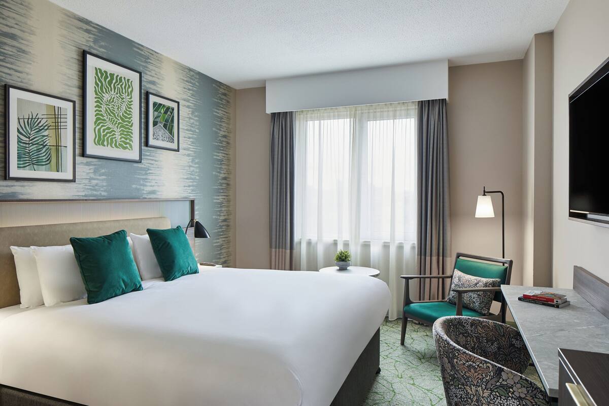 A hotel room with a large bed, a desk, a chair, and a TV.