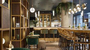 A bar area with multiple seating options, including round tables and bar stools, and a bar counter with a variety of bottles. - Leonardo Royal Hotel Glasgow (Glasgow)