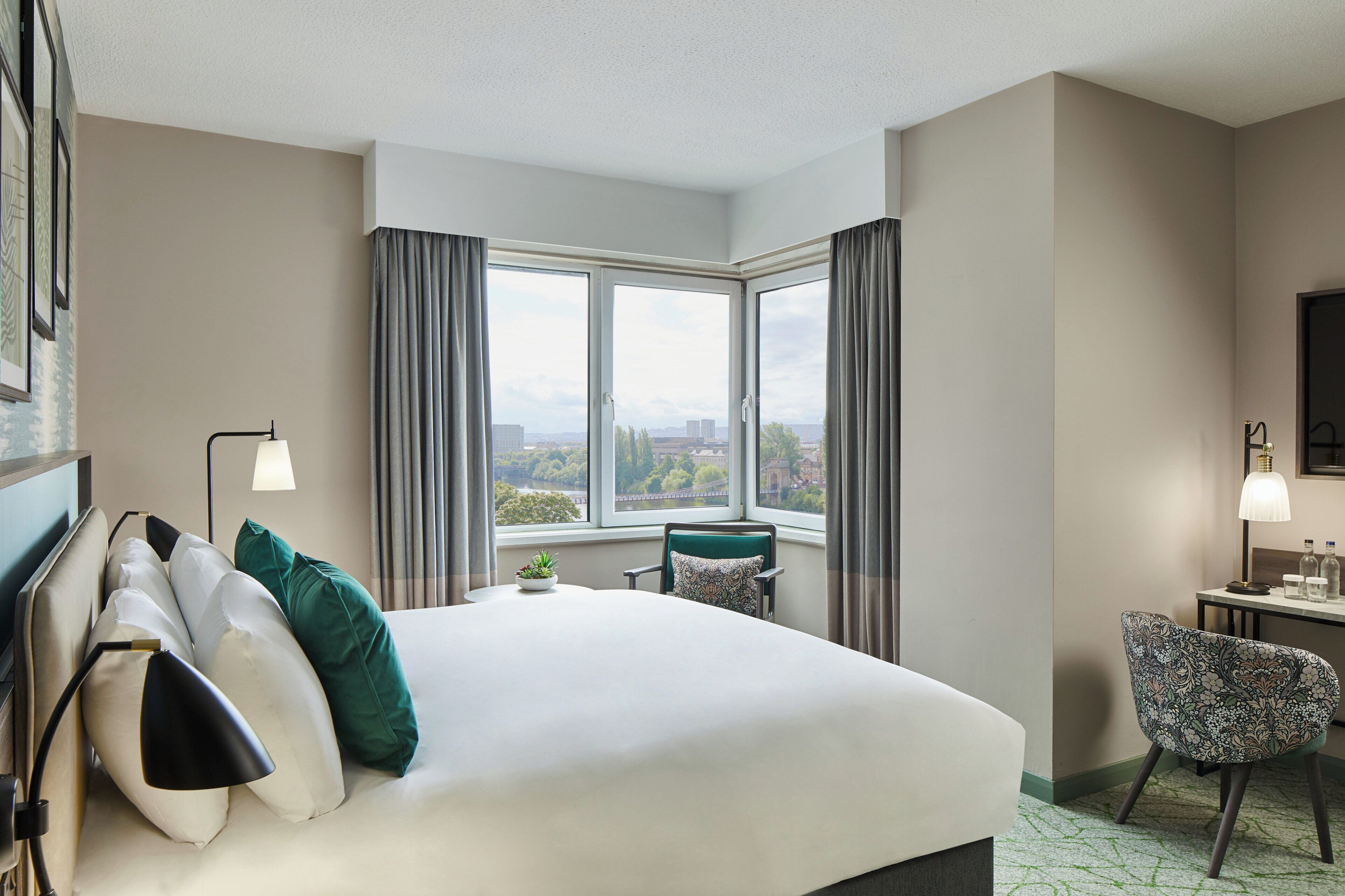 Een hotelkamer met een groot bed, een bureau, een stoel en een raam met uitzicht op de stad.