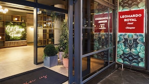 The entrance of the Leonardo Royal Hotel in Glasgow, featuring a modern glass facade, a welcoming neon sign, and a decorative rose pattern on the wall. - Leonardo Royal Hotel Glasgow (Glasgow)