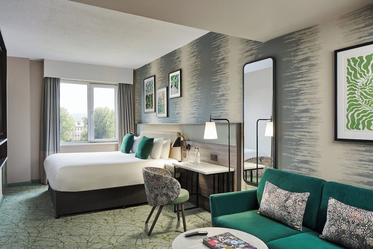 A hotel room with a large bed, a desk, a green sofa, and a mirror.