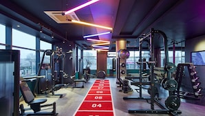 A gym with various exercise equipment, a red running track, and large windows offering a city view. - Leonardo Royal Hotel Glasgow (Glasgow)