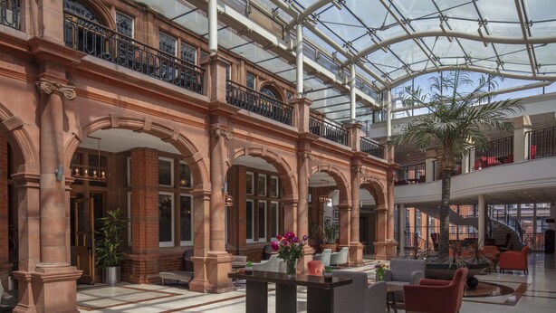 Eine geräumige Lobby mit Glasdecke, mehreren Ebenen und einer zentralen Sitzgruppe mit modernen Möbeln.