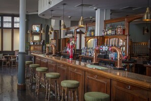 A bar with wooden stools, a bar counter, and a variety of bottles and glasses. - The Crown London, WorldHotels Distinctive (London)