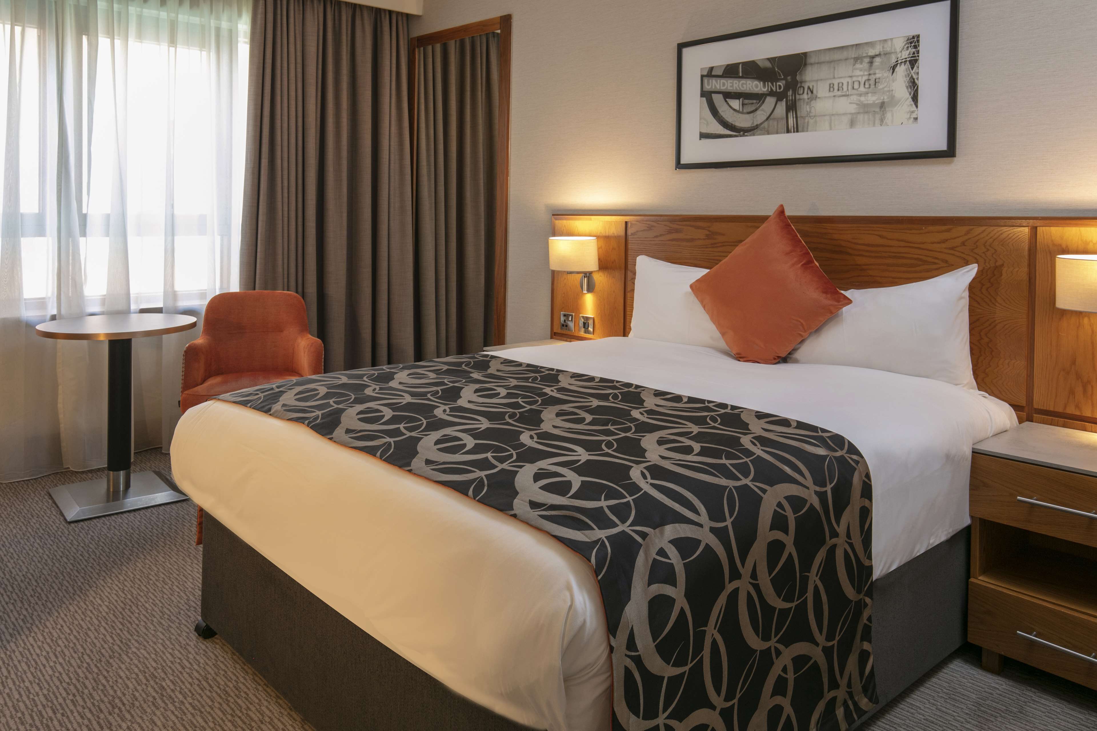A hotel room with a large bed, a bedside table, a chair, and a small table.