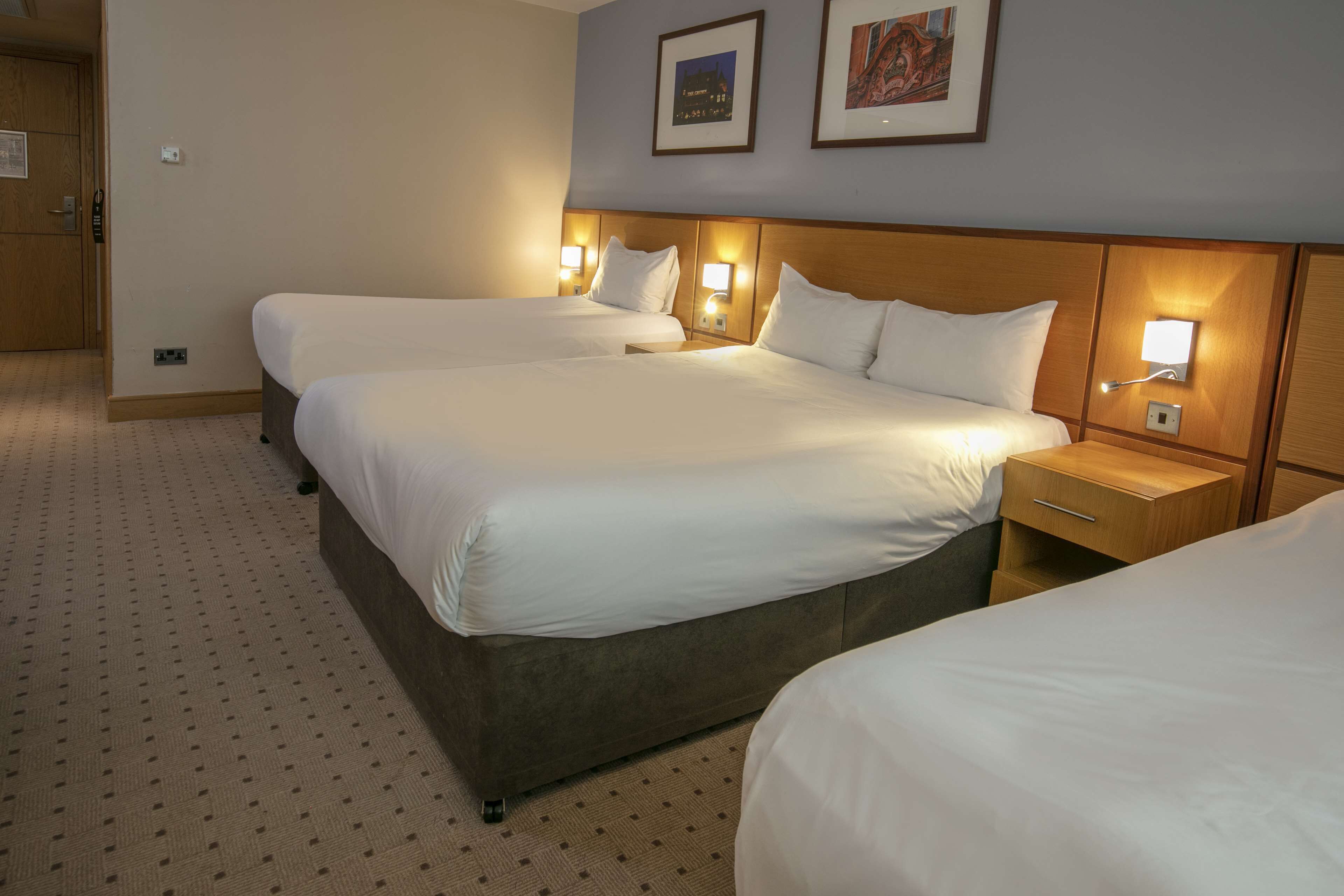 Une chambre d’hôtel avec deux lits, une tête de lit en bois, des lampes de chevet et un sol recouvert de moquette.