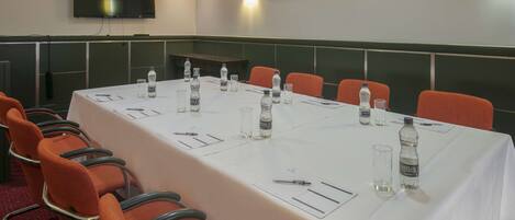 A conference room with a long table, orange chairs, water bottles, and a flat-screen TV on the wall.
