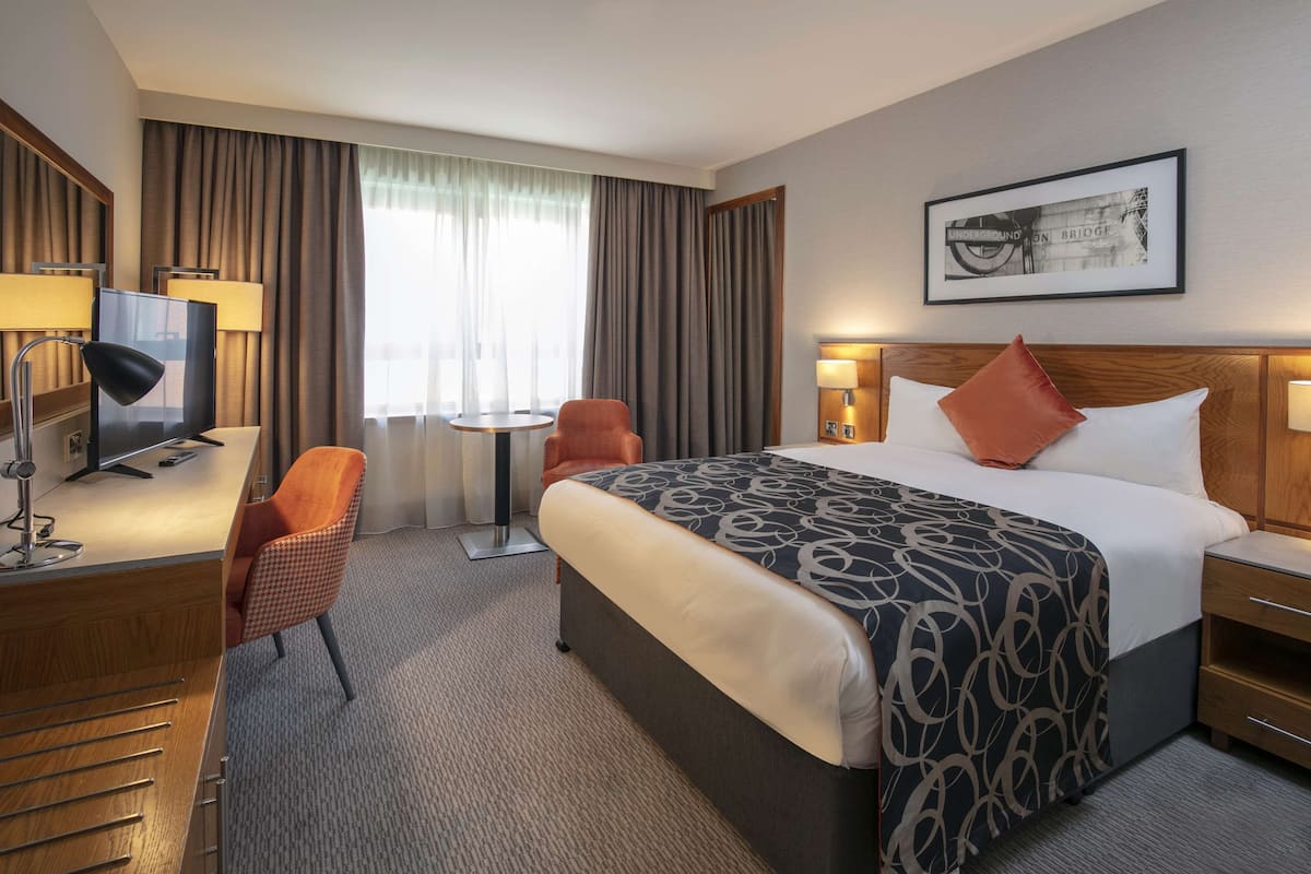 A hotel room with a large bed, a desk with a computer, a chair, and a small table.