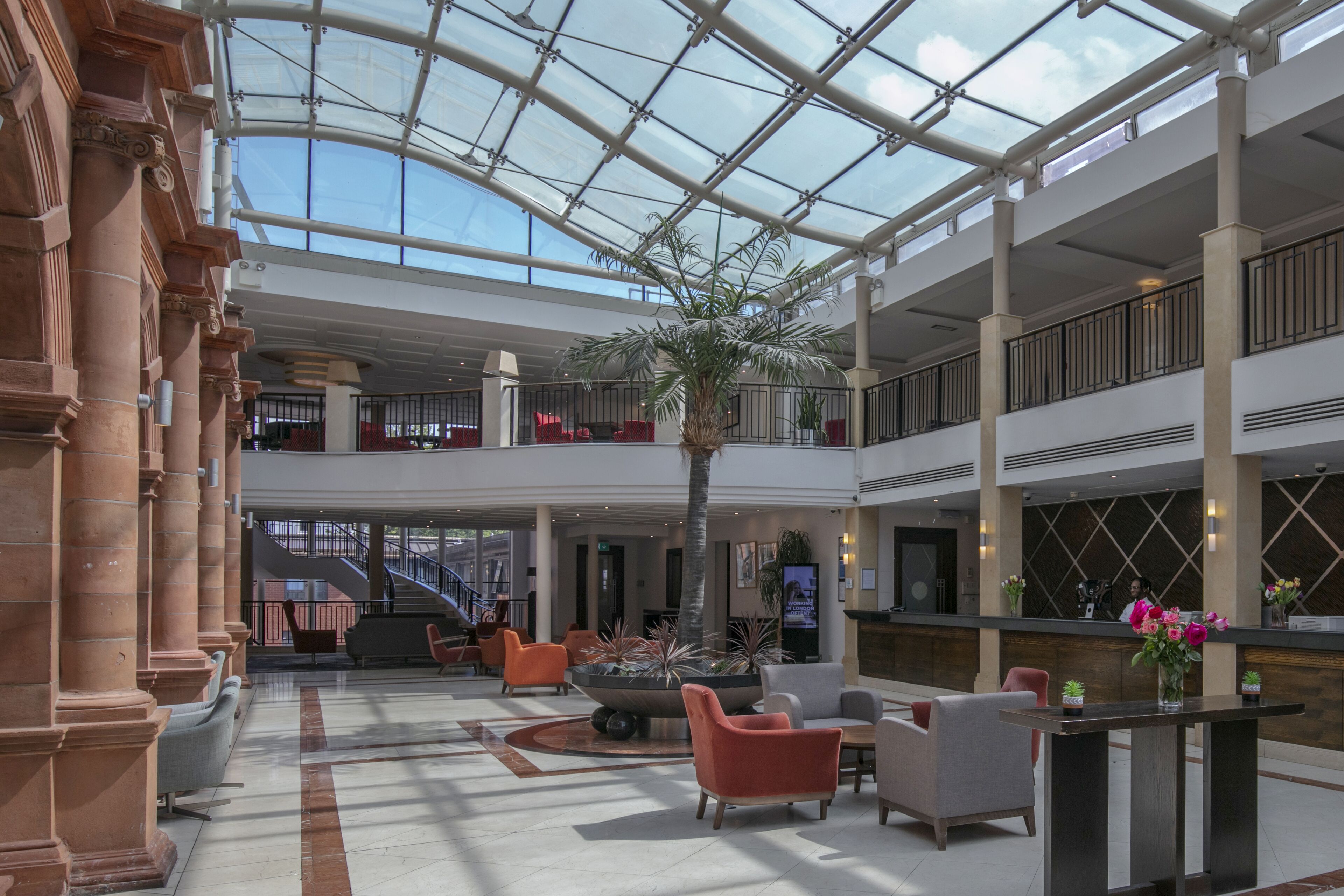 A spacious atrium with a glass ceiling, multiple seating areas, and a reception desk.