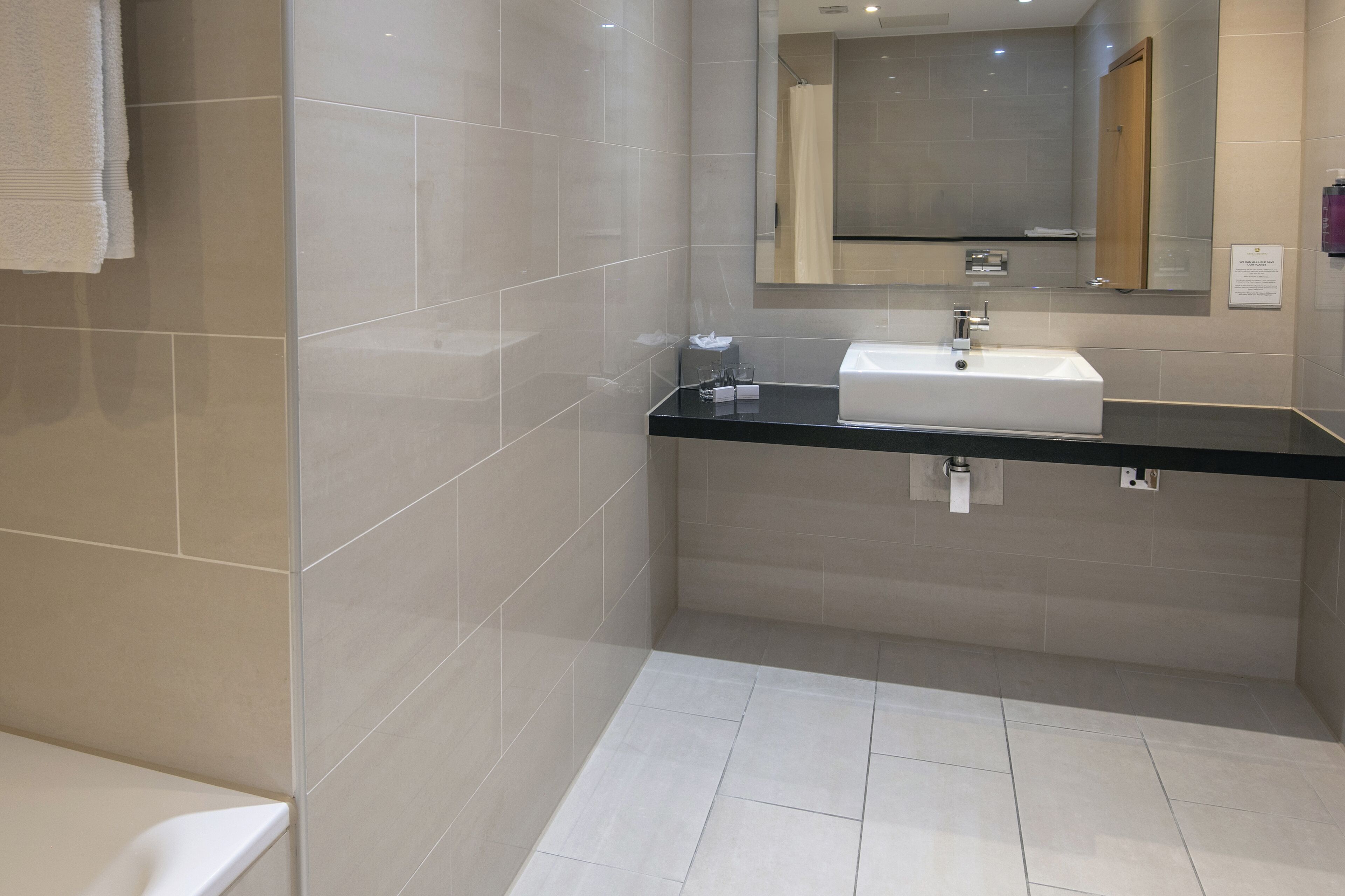 A modern bathroom with a white sink, black countertop, and beige tiles.