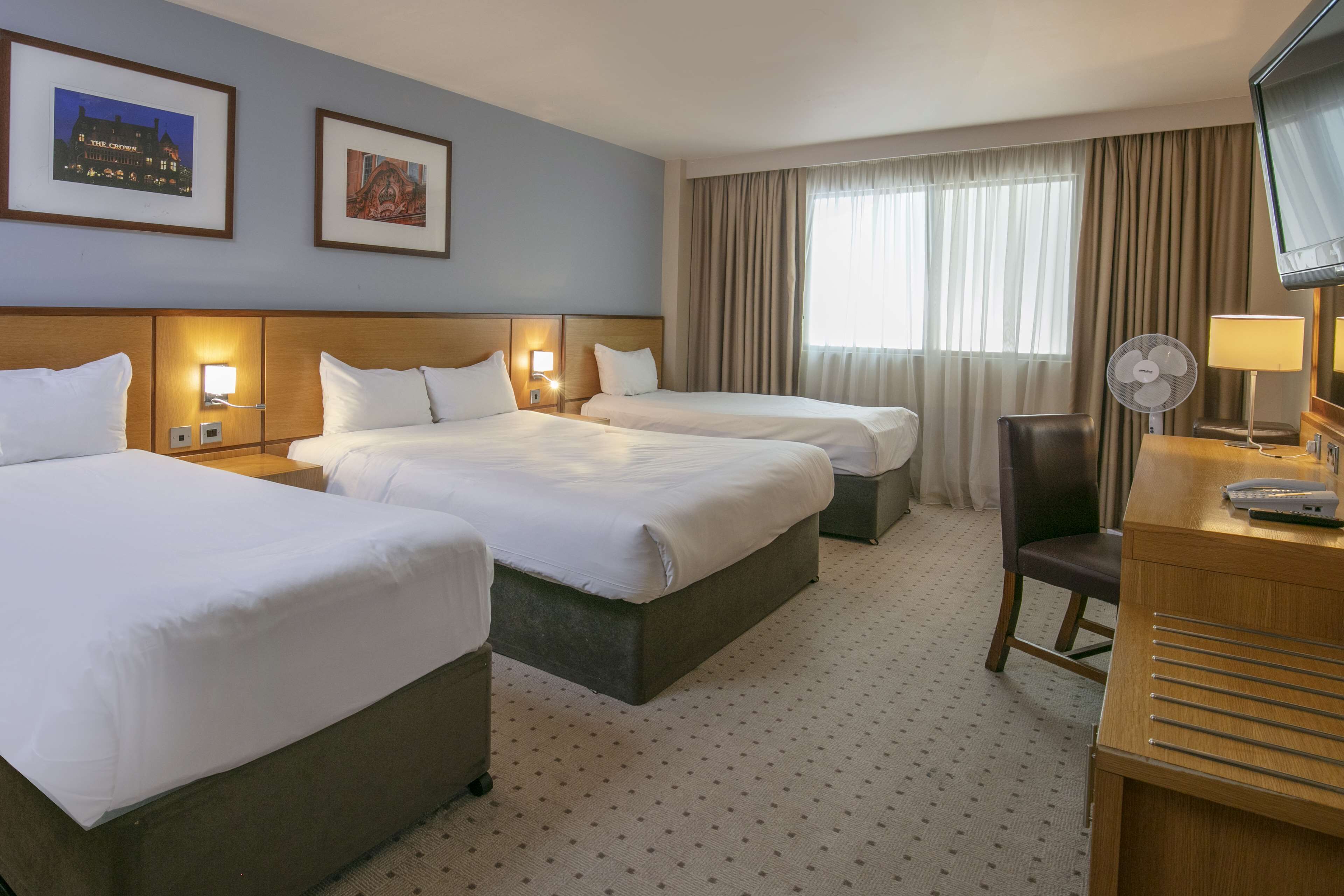 A hotel room with two beds, a desk with a lamp, a chair, and a TV.