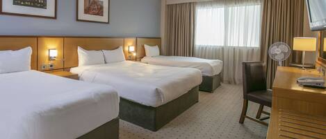 A hotel room with two beds, a desk with a lamp, a chair, and a TV.