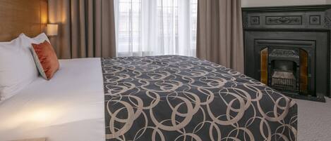 A hotel room with a large bed, a fireplace, and a view through sheer curtains.