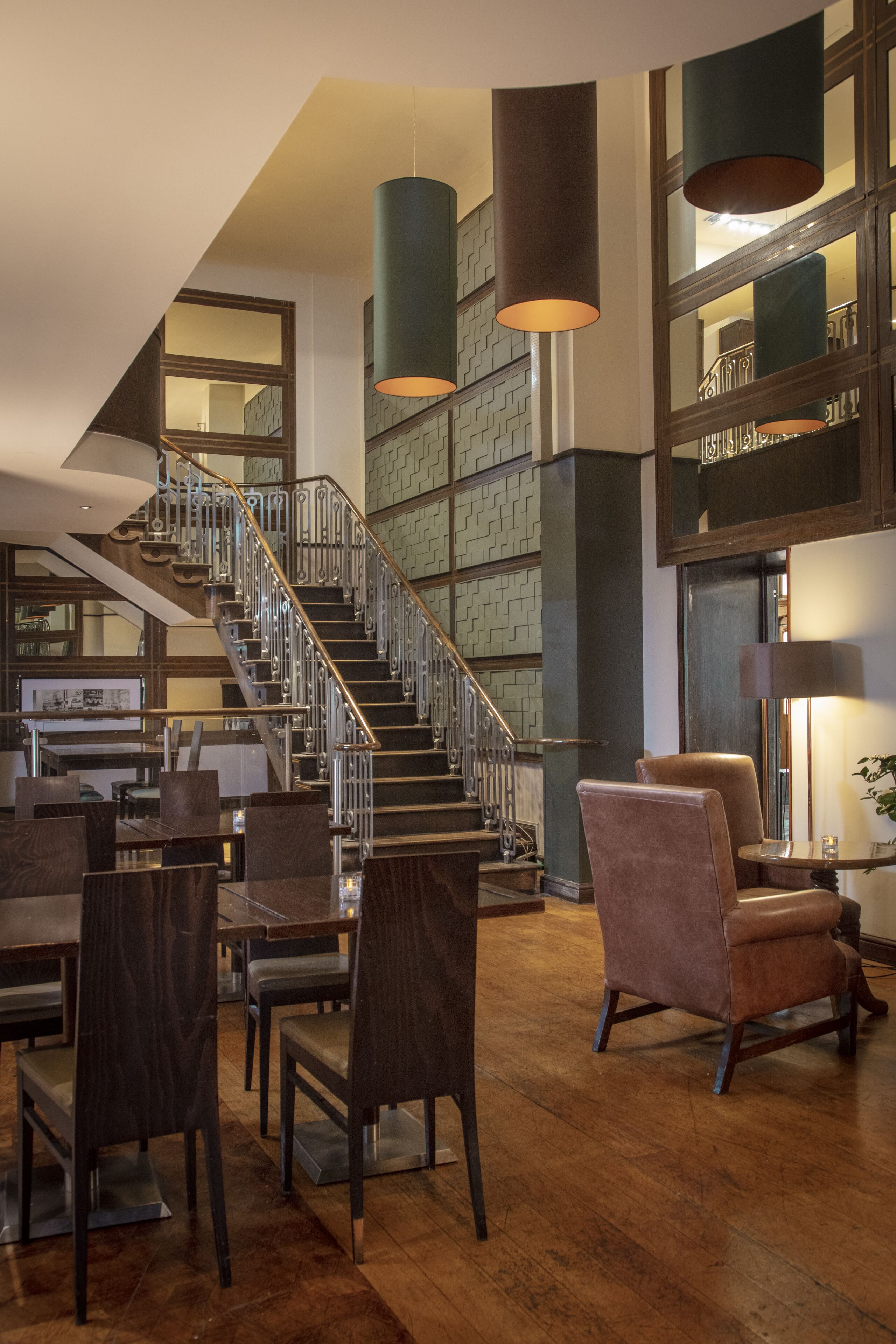 A spacious hotel lobby with a modern staircase, wooden flooring, and contemporary furniture.
