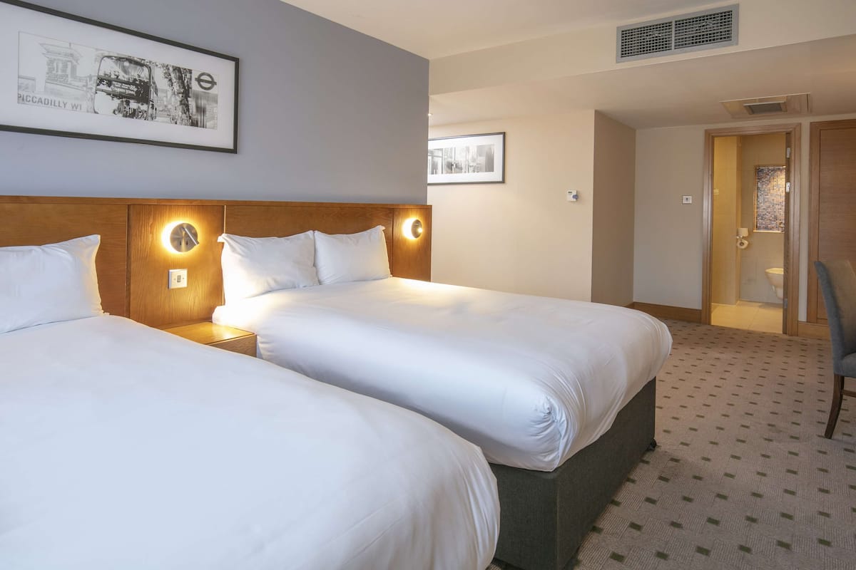A hotel room with two beds, a wooden headboard, a framed picture on the wall, and a patterned carpet.