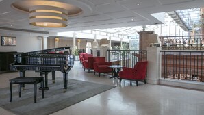 Eine geräumige Lobby mit einem Flügel, roten Polstersesseln und einer modernen Kronleuchter.