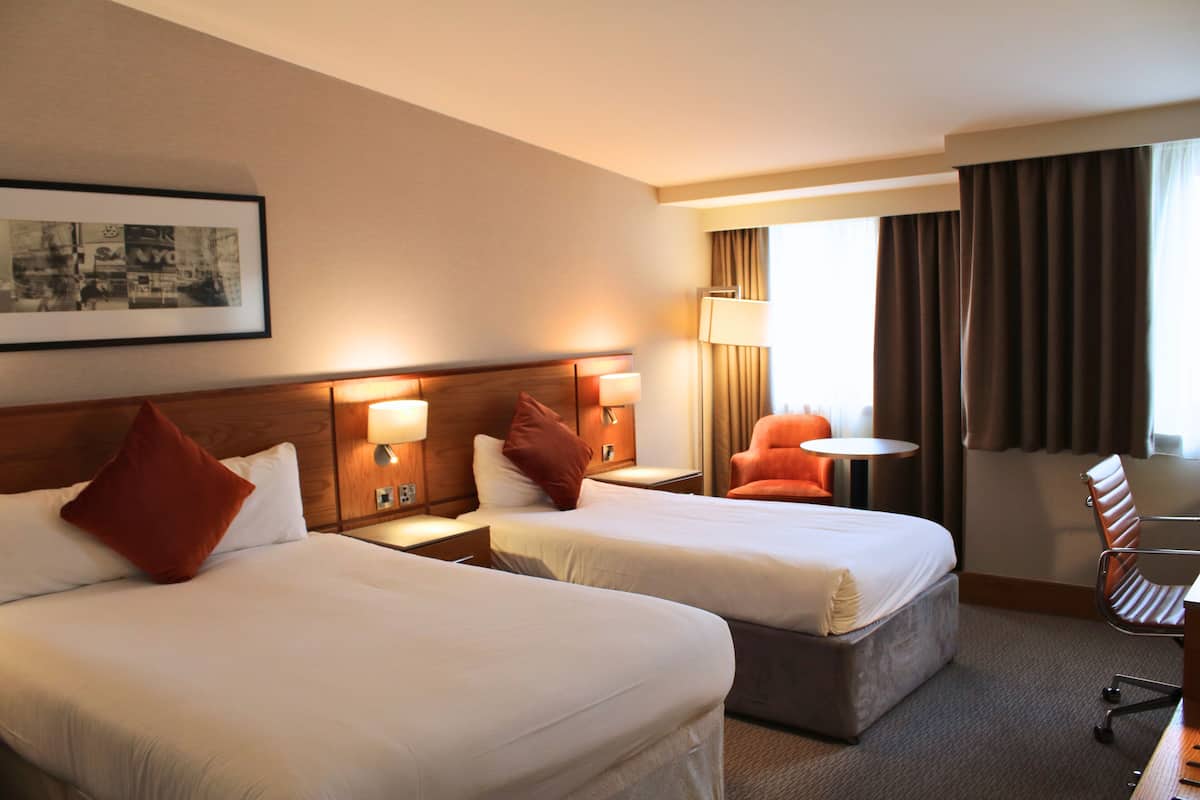 A hotel room with two beds, a desk, a chair, a lamp, and a window with curtains.